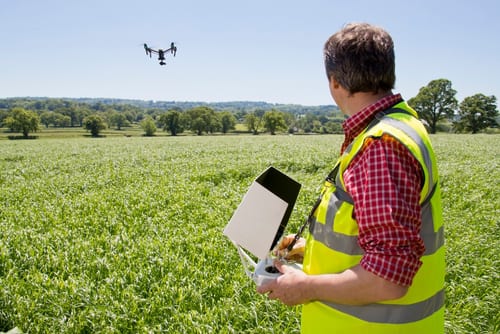 An operator in a hi-vis vest flying a drone with a handheld controller in a field